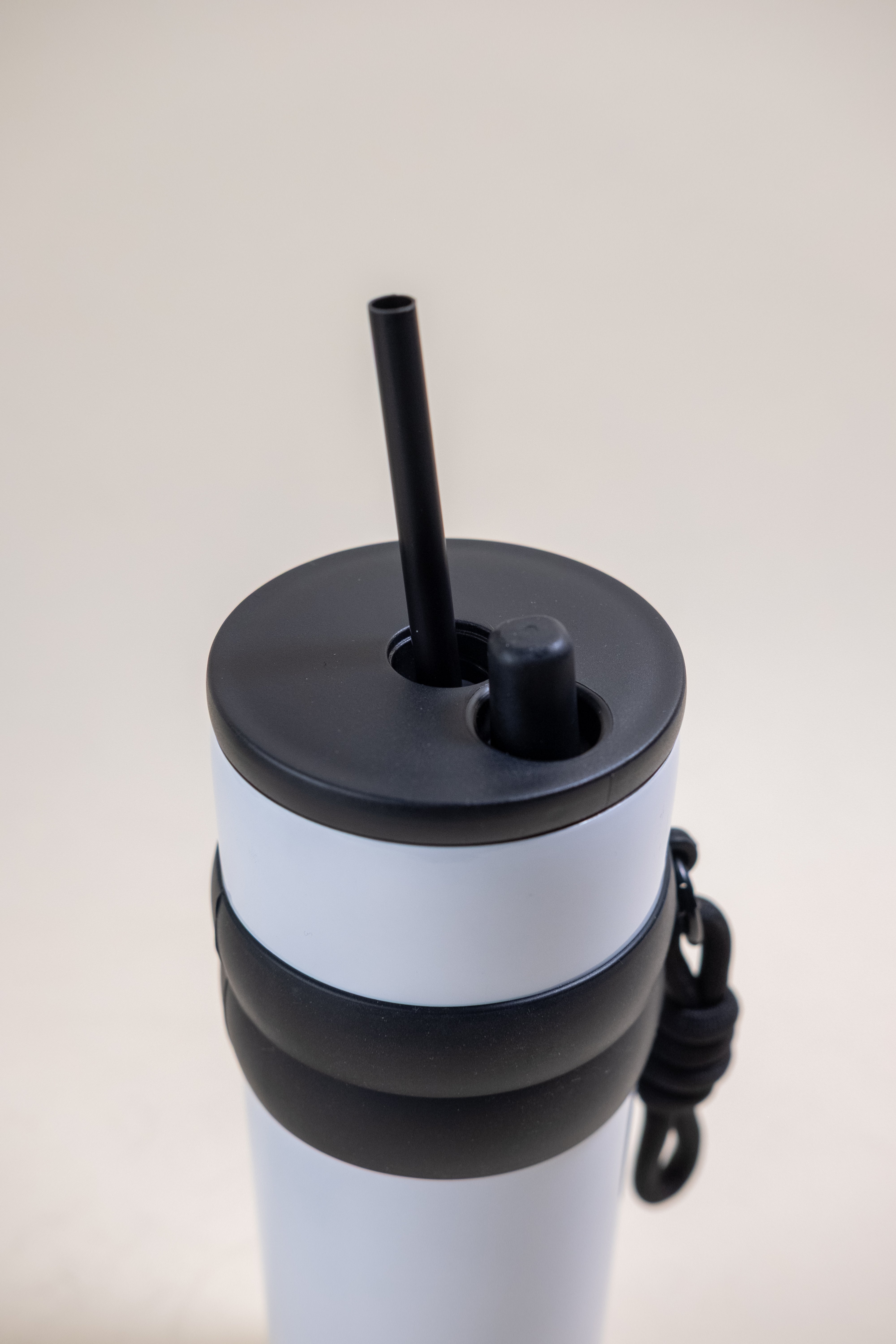 Close-up view of the top part of a white and black stainless steel straw tumbler, showcasing the black lid with a BPA-free plastic straw and a black rubber grip band, emphasizing its sleek design and user-friendly features.