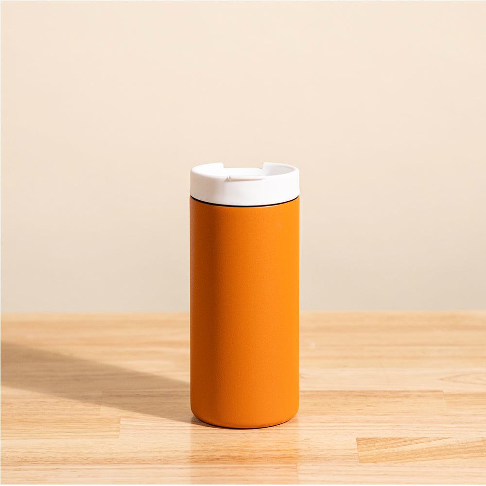 LAMOSE Grouse 12 oz insulated tumbler in matte orange, featuring a white flip-top lid, shown from a front angle on a wooden surface.