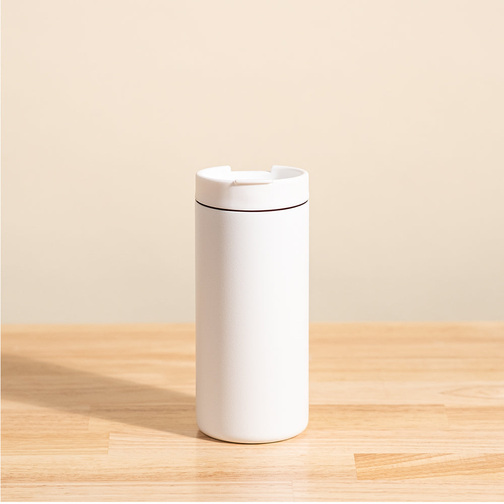 LAMOSE Grouse 12 oz travel tumbler in matte white, with a flip-open lid, shown from the front on a wooden surface.