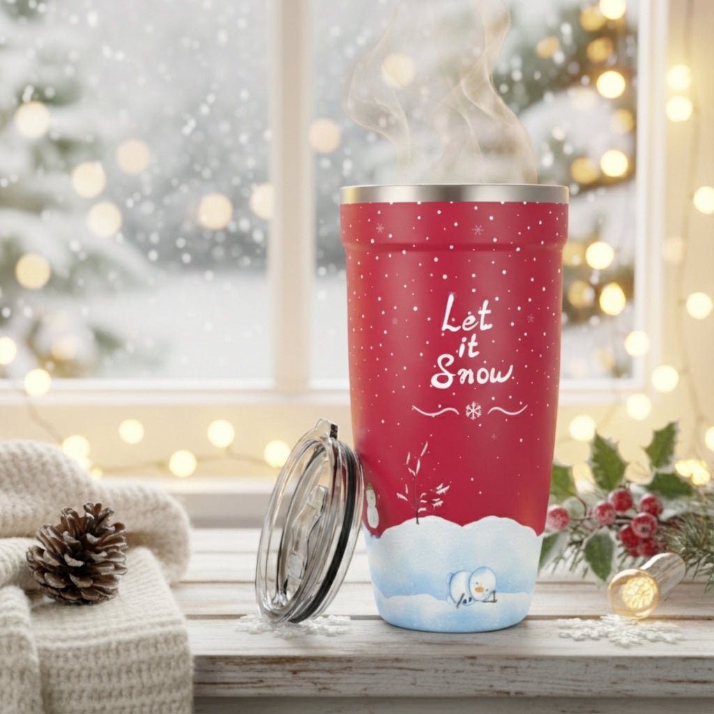 Lifestyle shot - Red 16oz stainless steel tumbler with white Let It Snow script, snowflakes, and snowmen design on a wooden table with holiday decor