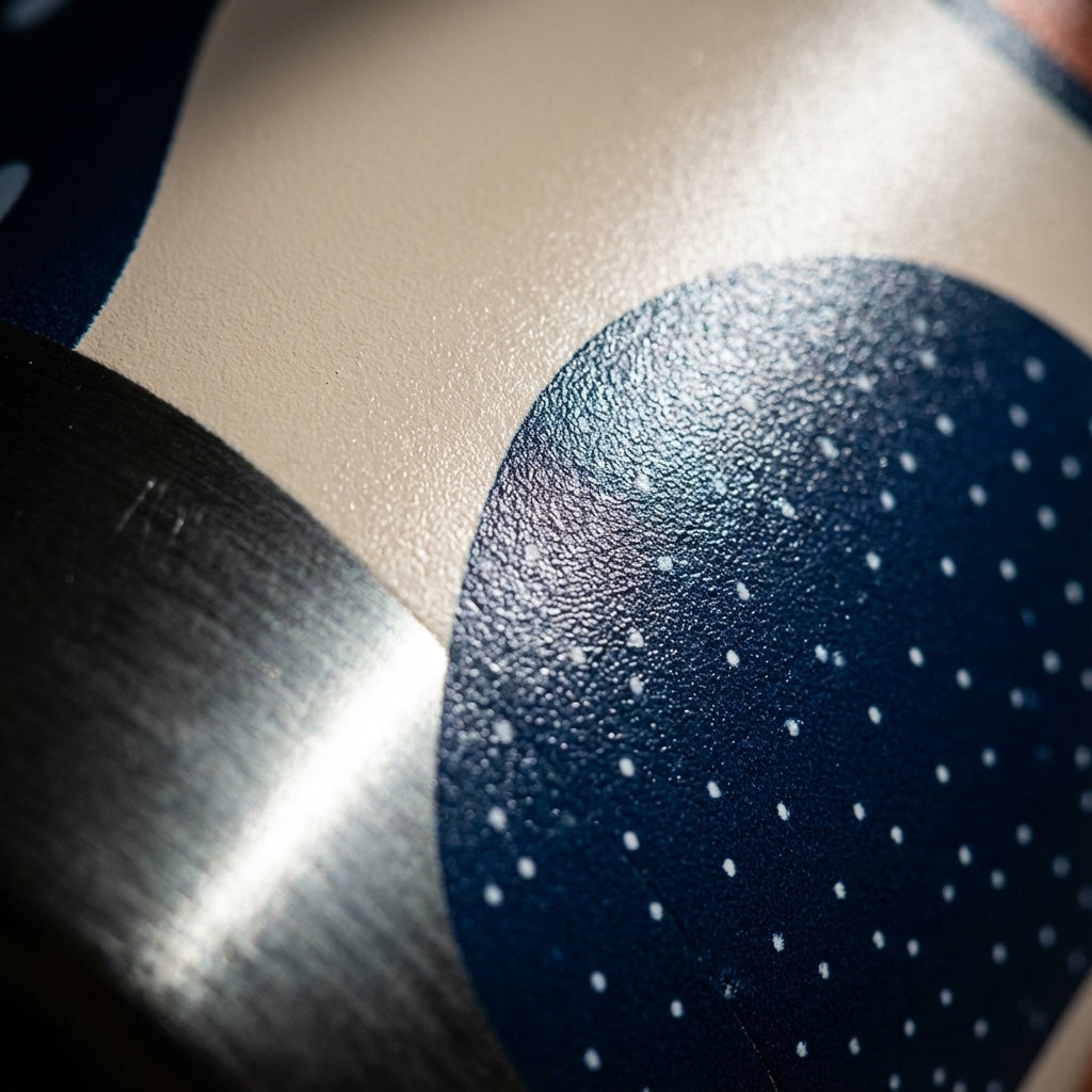 Detail shot - Logan Pro 16 oz stainless steel tumbler featuring an organic abstract pattern with navy, orange, and beige shapes sitting on a wooden cafe table.