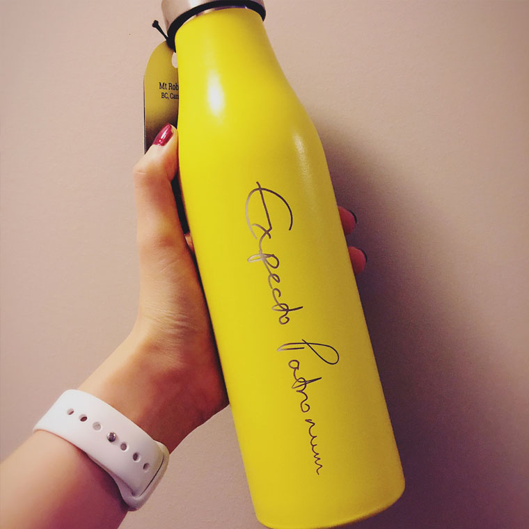LAMOSE personalized yellow stainless steel water bottle with custom engraving. A hand with a white smartwatch holds the premium bottle, close-up.
