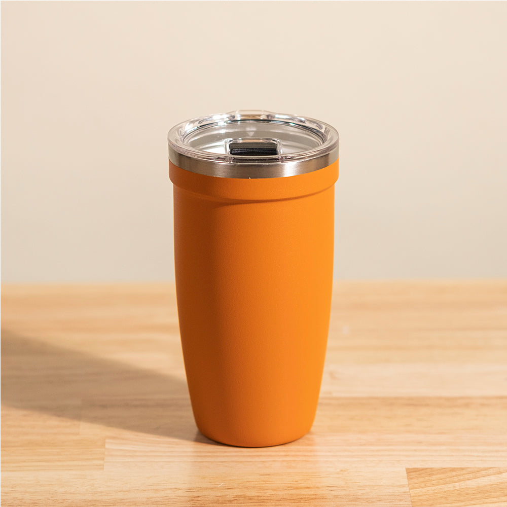 LAMOSE Peyto 16 oz tumbler in matte orange, front view. Features a clear lid with silver rim and dark slider, sitting on wood.