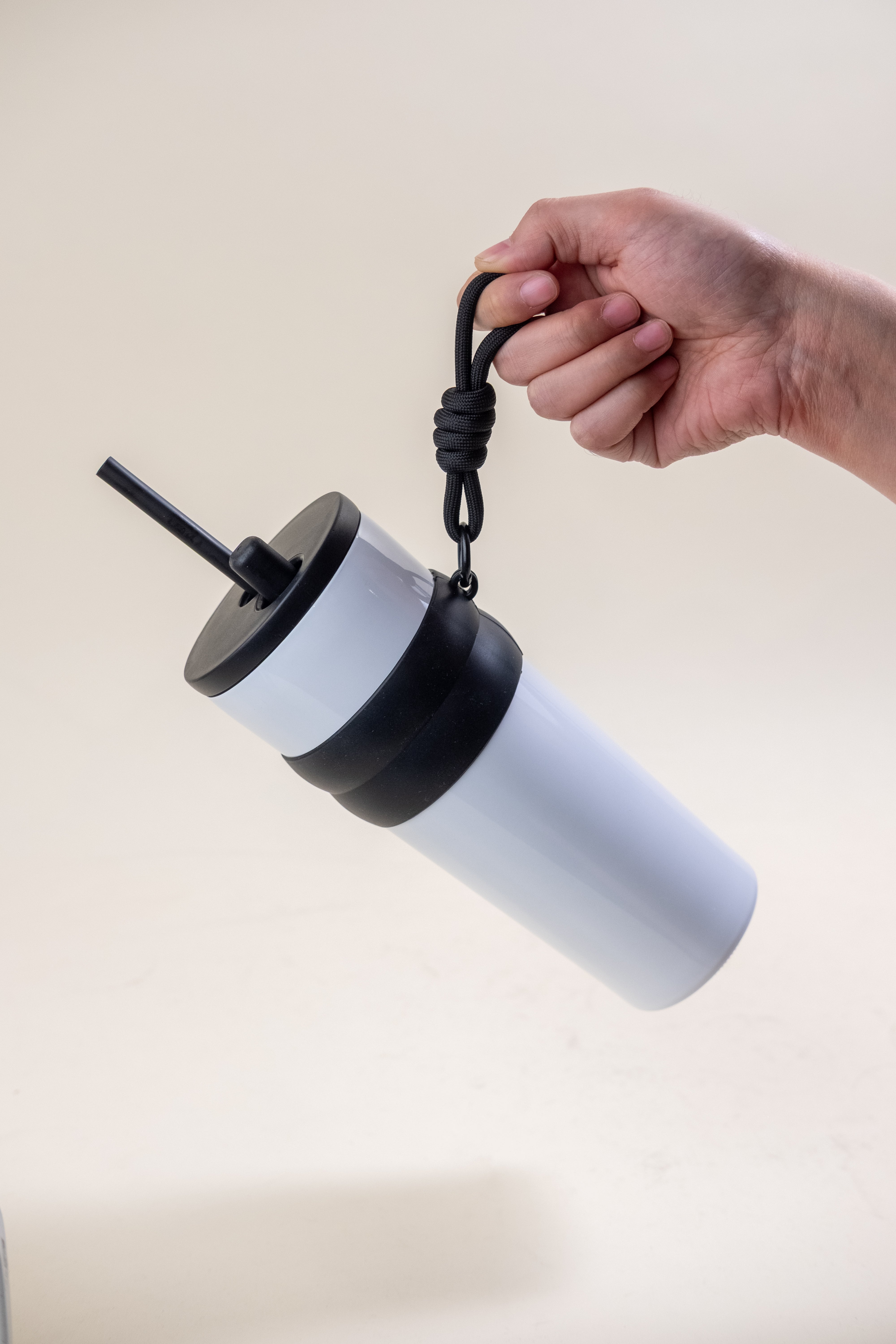Hand holding a portable stainless steel straw tumbler with a two-tone black and white design, featuring a rubber holder and BPA-free plastic straw, ideal for on-the-go hydration and personalization.