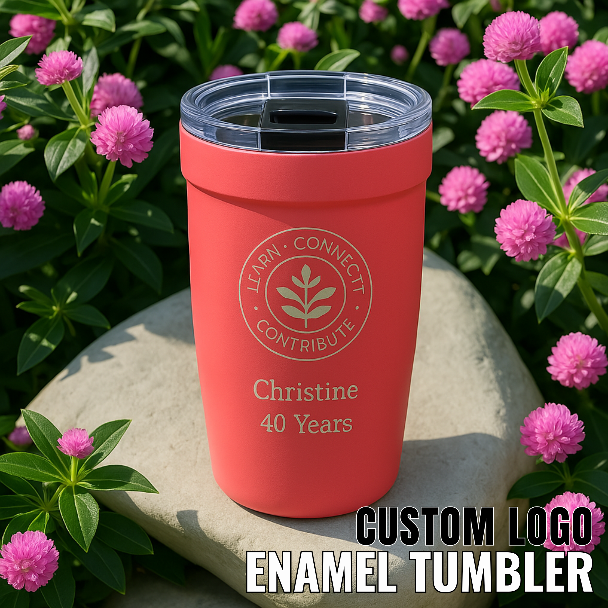 LAMOSE Peyto Pro Enamel 12oz ruby-red tumbler, standing on a stone with pink flowers. Features custom engraved logo, name, and clear lid.