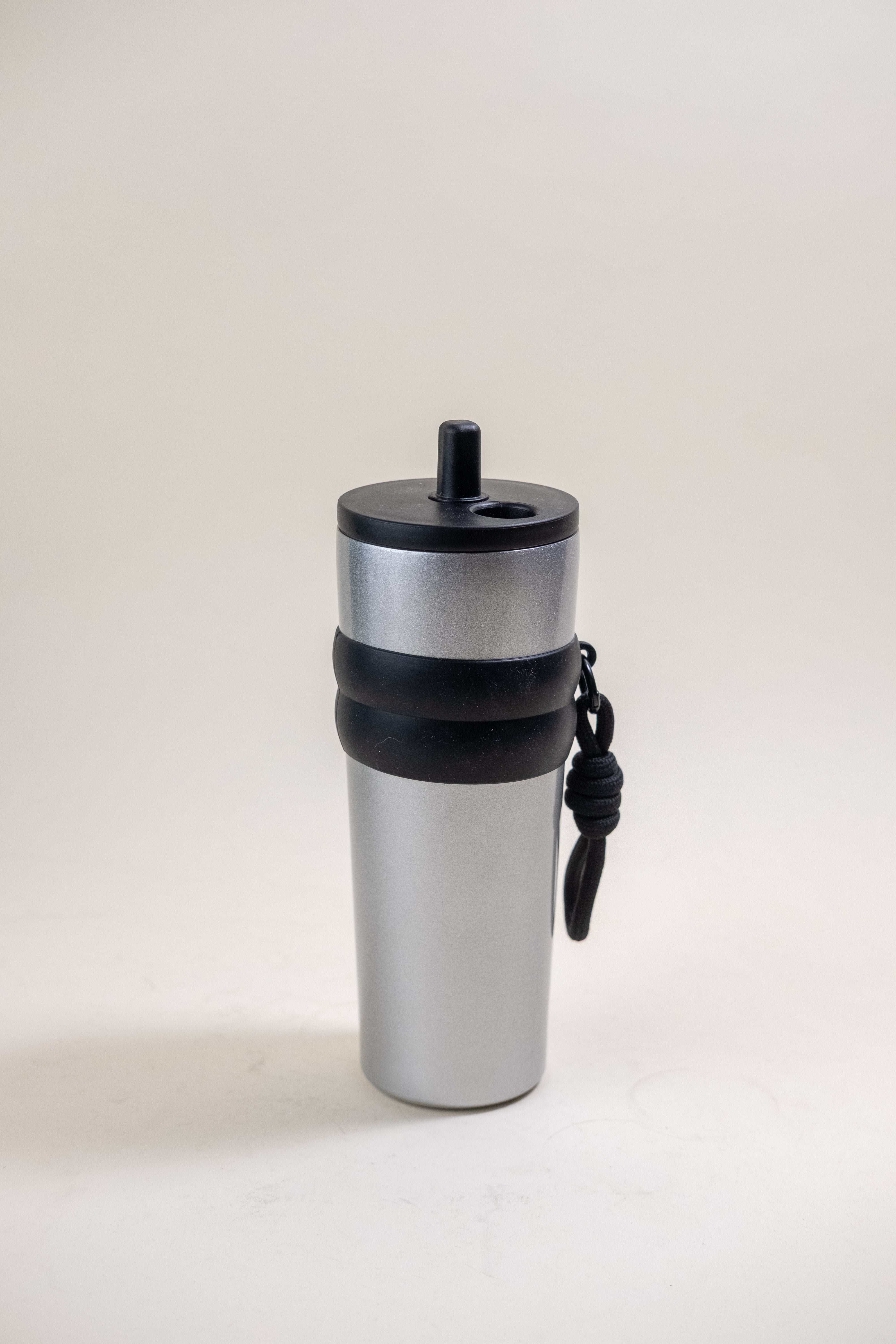 Silver stainless steel straw tumbler with a black lid and rubber grip, featuring a BPA-free black plastic straw and a durable carrying rope, ideal for both style and practical use.