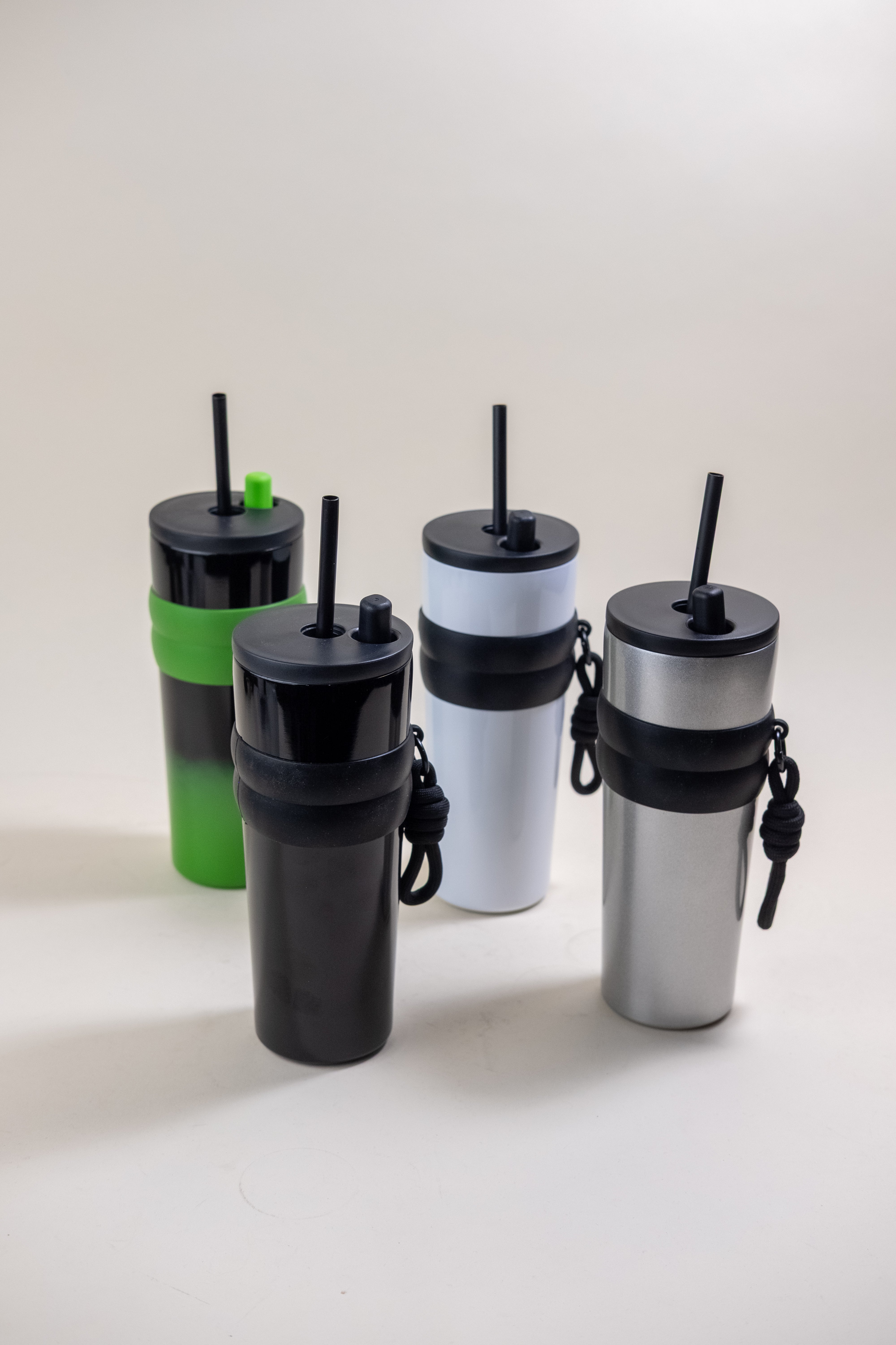 An array of stainless steel straw tumblers in assorted colors including black, green, white, and silver, each featuring a BPA-free plastic straw and a convenient rubber grip. These tumblers are designed for easy customization and portability, suitable for both hot and cold beverages.