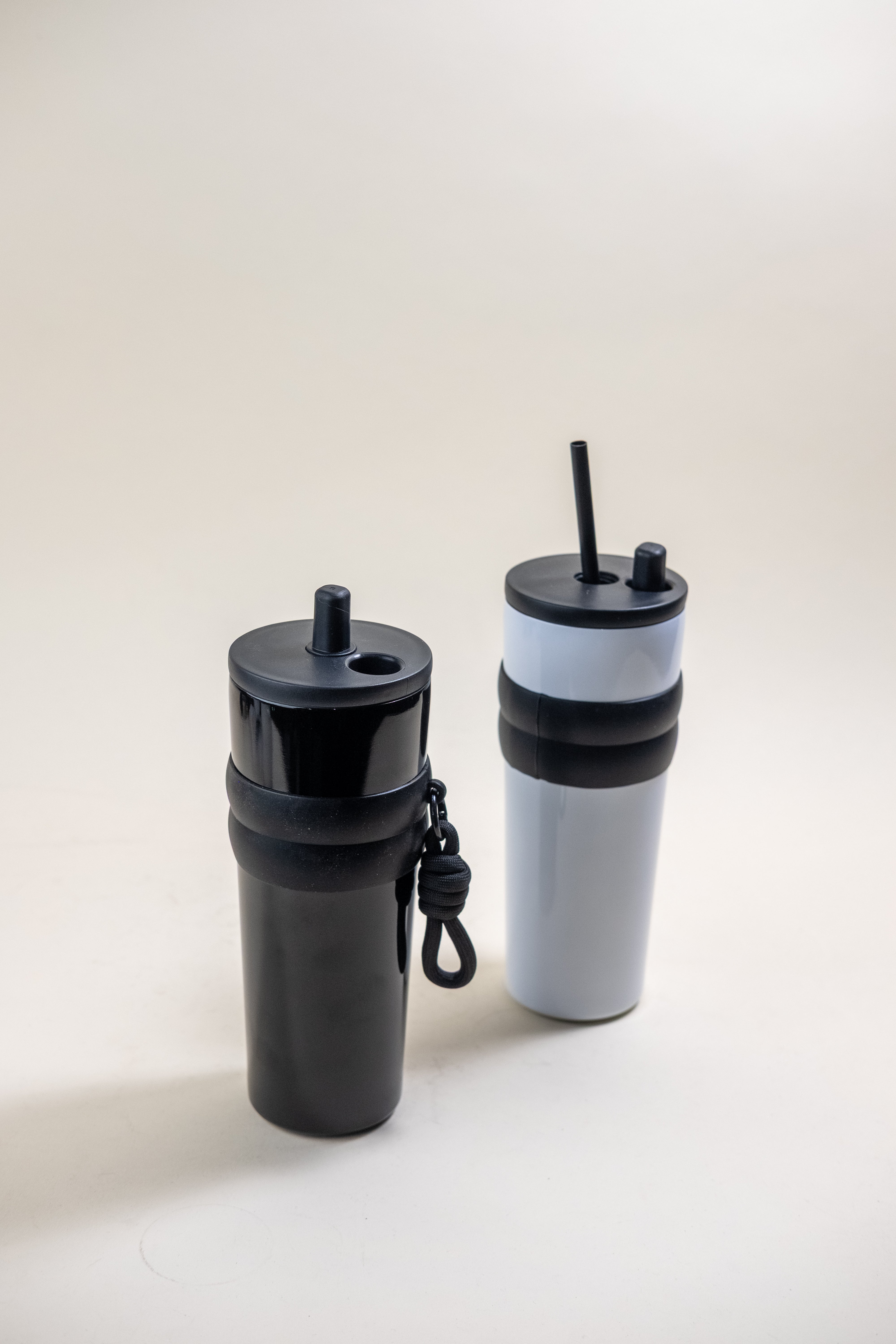 Two stainless steel straw tumblers, one in matte black and another in two-tone black and white, each equipped with BPA-free plastic straws and rubber holders, ideal for personalized engravings and daily use.