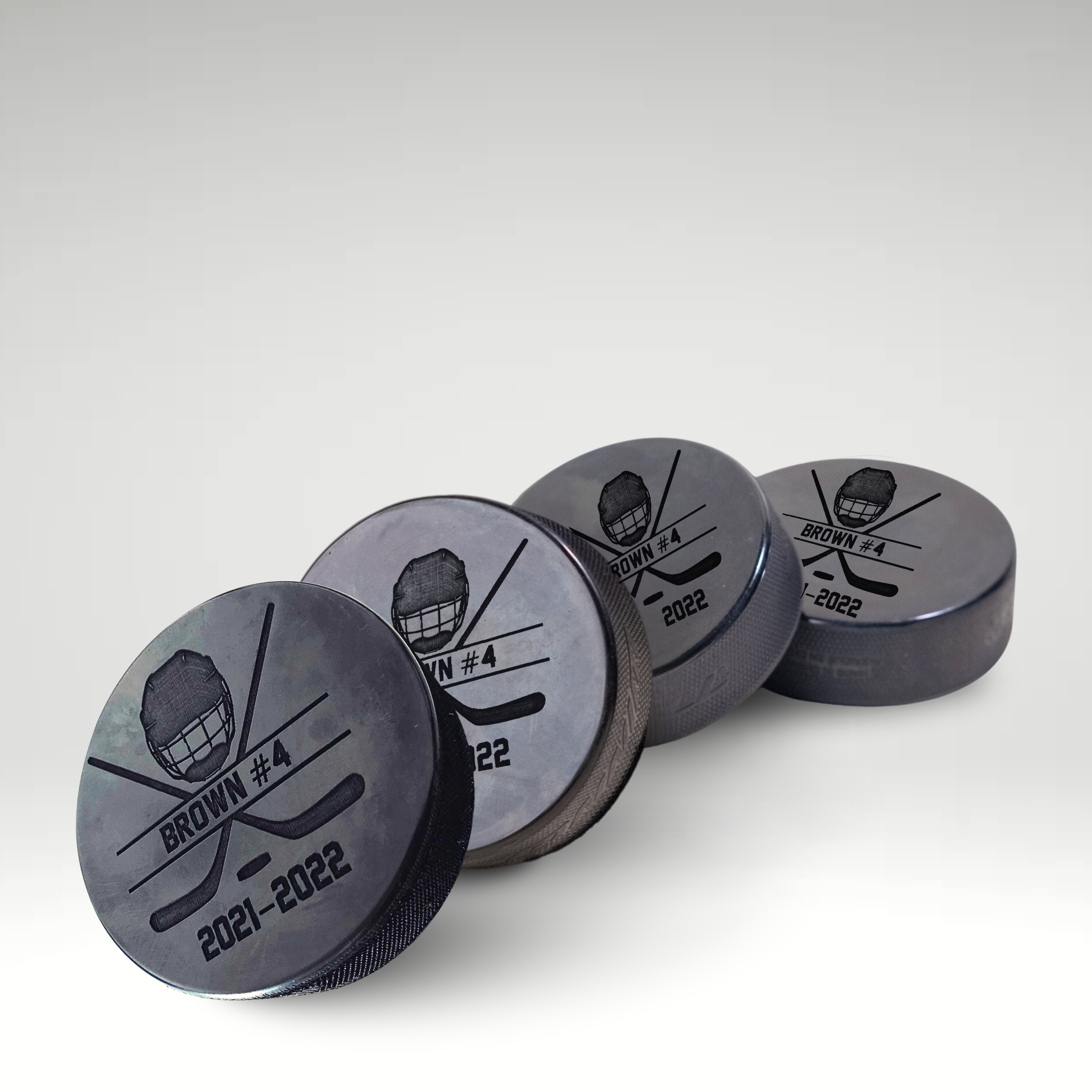 Custom engraved hockey pucks with player name and number, featuring a helmet and crossed sticks design.