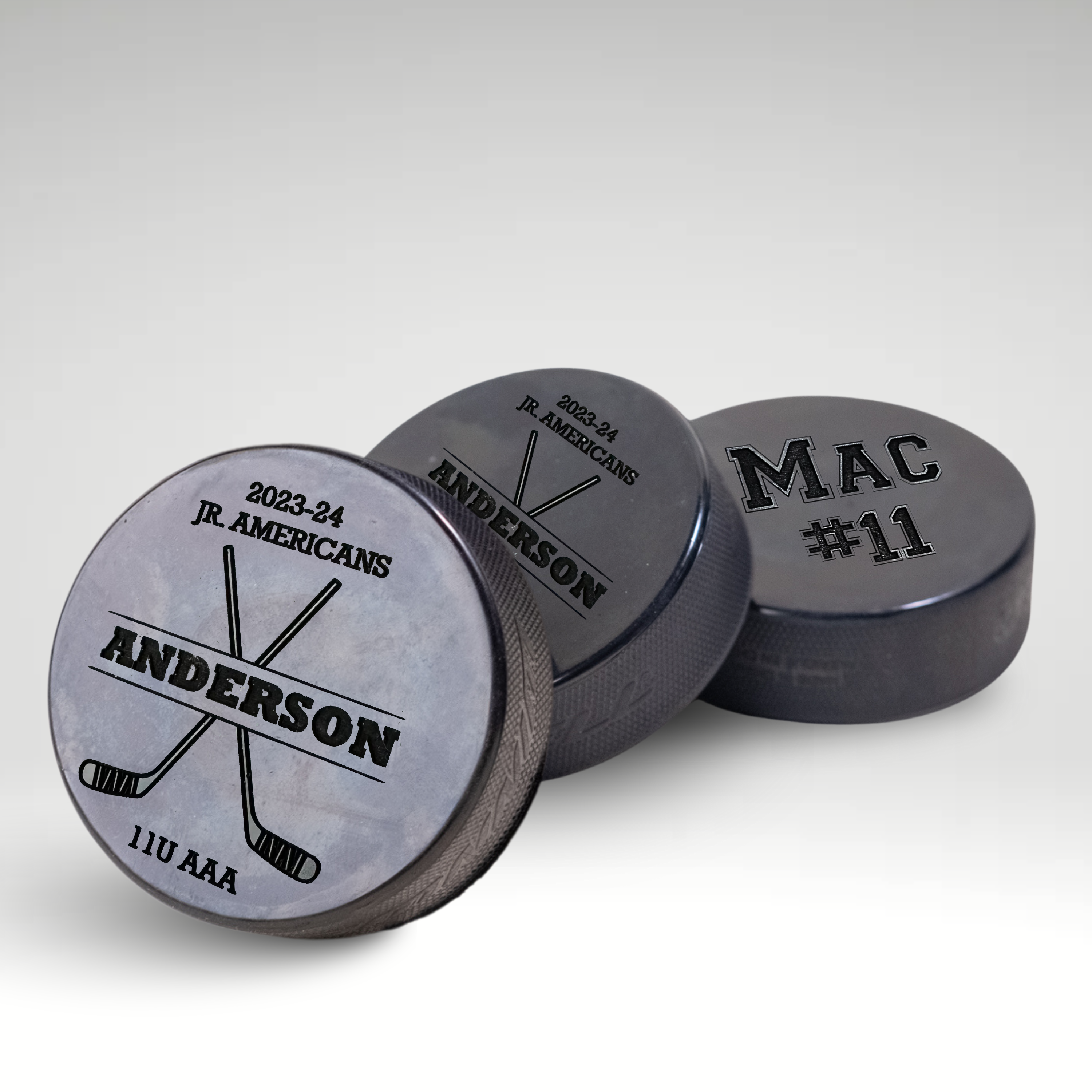 Personalized engraved hockey pucks for Jr. Americans 11U AAA team featuring player names and numbers.