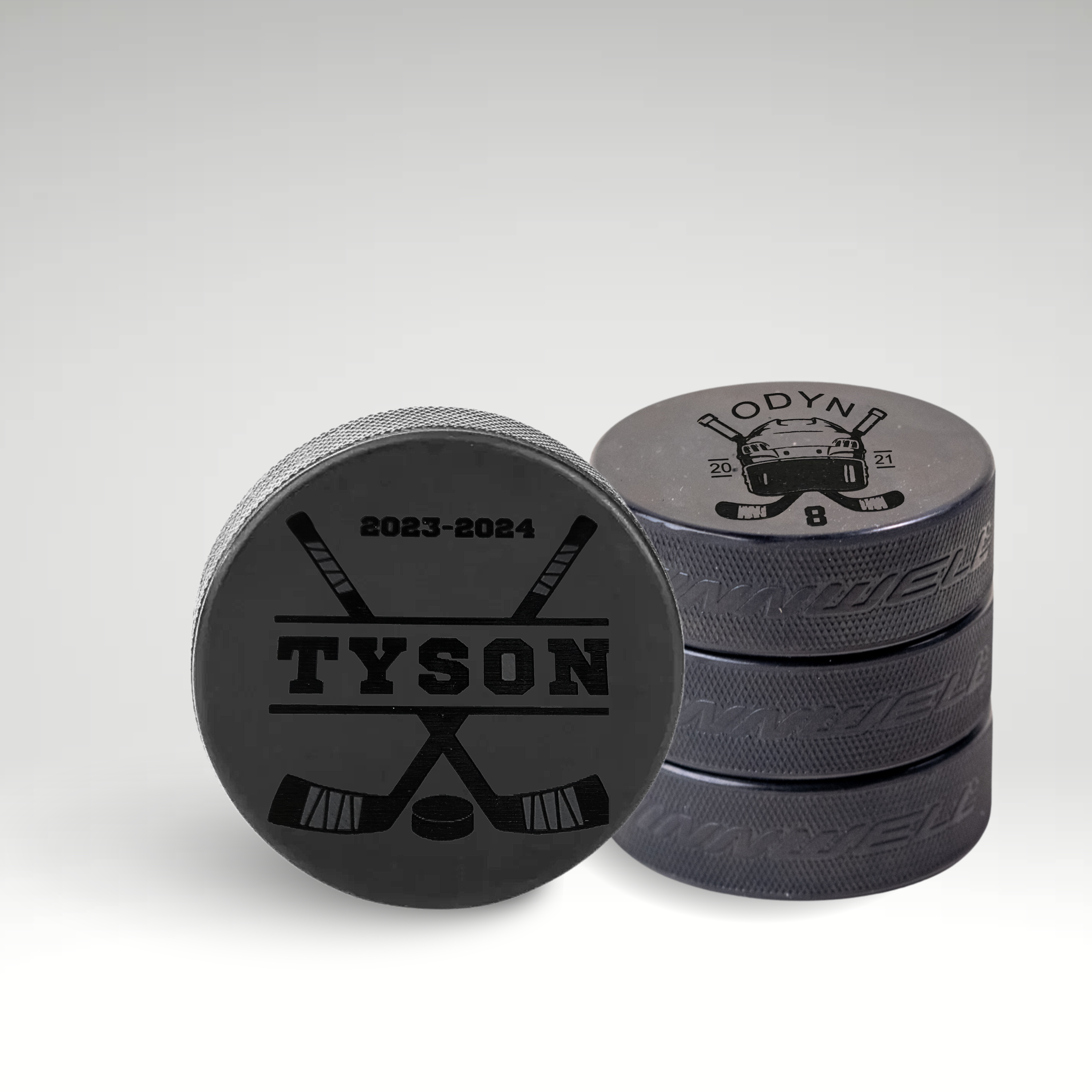 Custom engraved hockey pucks featuring personalized player names, numbers, and crossed sticks design.