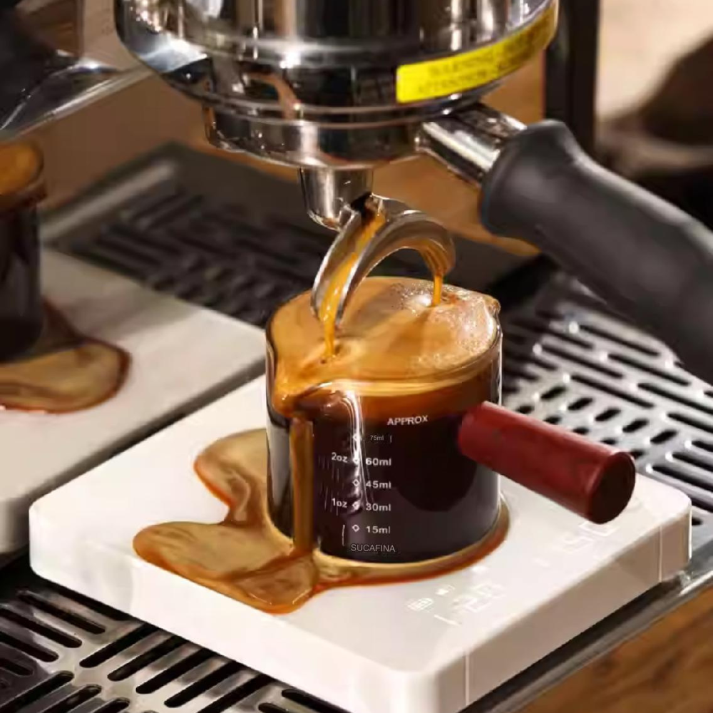Espresso overflowing from a glass shot cup with a red handle on a white digital coffee scale, capturing a rich crema during an extraction from a professional espresso machine. #color_black