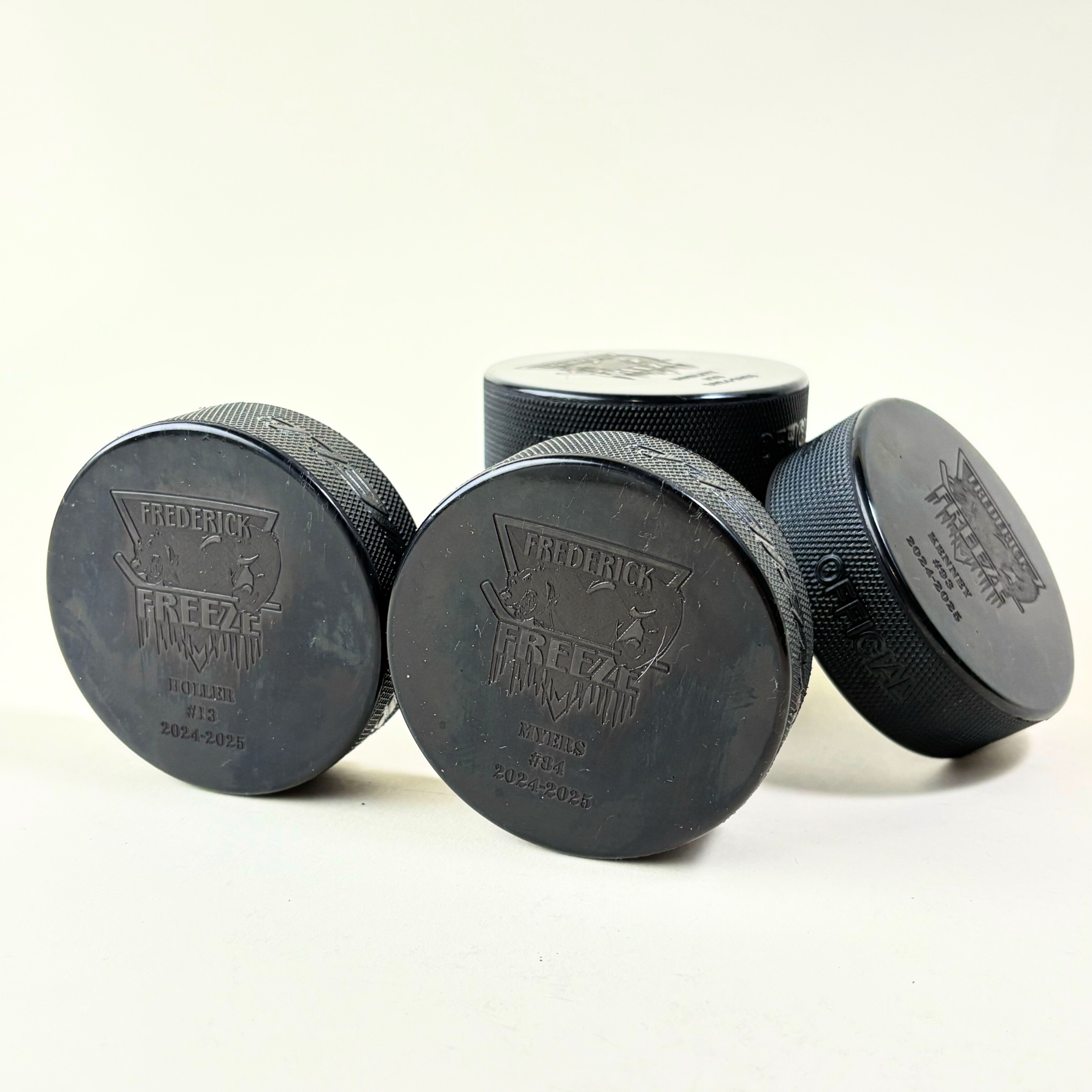 Set of custom engraved hockey pucks for the Frederick Freeze team, featuring player names, numbers, and the 2024-2025 season.