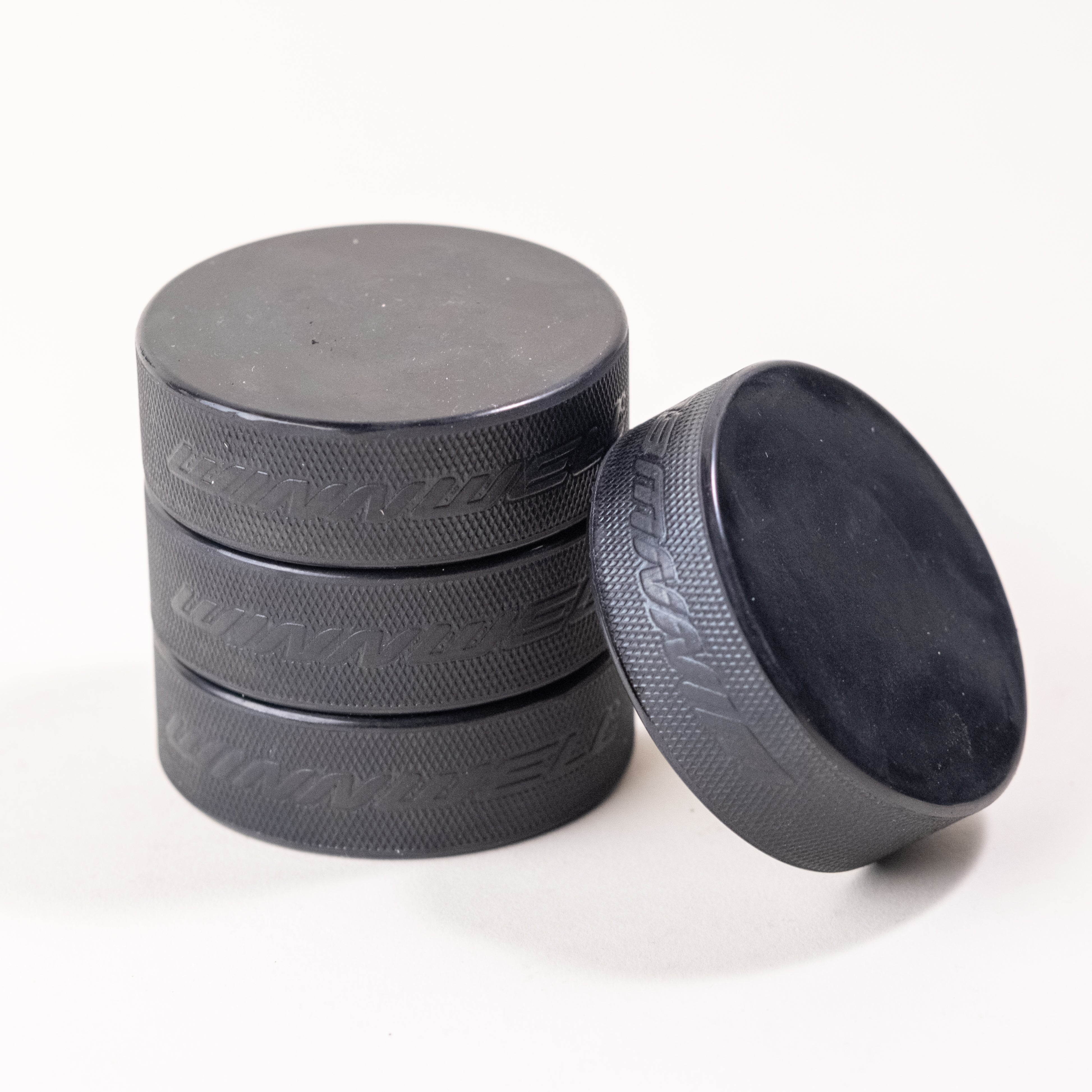 Stack of official black hockey pucks with textured edges, ideal for games, training, and custom engraving. Durable and high-quality pucks for players and teams.