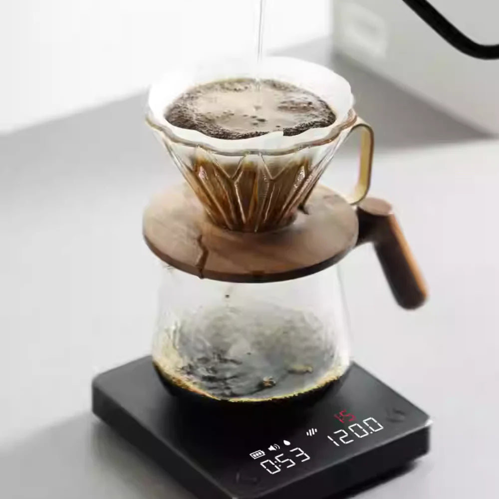 Pour-over coffee brewing with a glass dripper, wooden-handled server, and a digital coffee scale with a real-time weight and timer display for precision brewing.