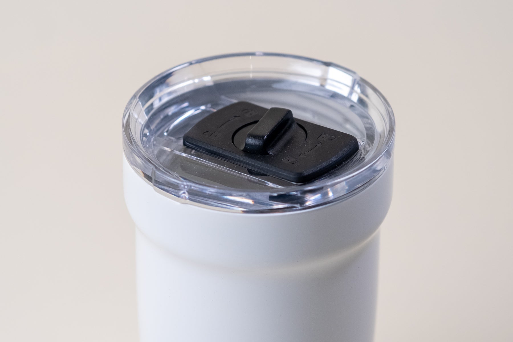 Close-up of a white enamel-coated insulated tumbler with a clear spill-resistant lid and black sliding lock. Durable stainless steel travel mug for hot and cold beverages.