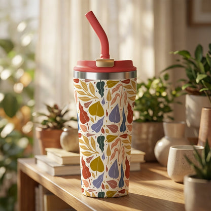 Cream 16oz insulated tumbler with red lid and straw featuring stylized gold, red, and green leaf pattern sitting on a rustic wooden surface.