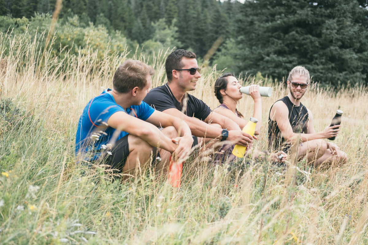 LAMOSE insulated water bottles in mint, yellow, and black, held by friends resting in a sunny outdoor field. Perfect for hydration.
