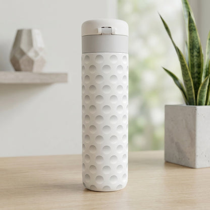 Close up of off-white Emerald 16 oz tumbler featuring a textured golf ball dimple pattern standing on a light wood surface.