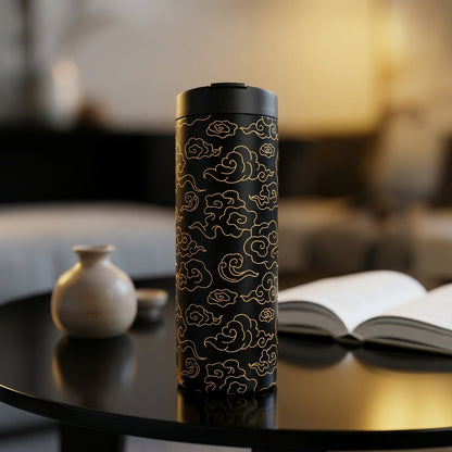 Matte black 16 oz insulated tumbler featuring a repeating golden Asian cloud pattern engraving, sitting on a wooden table.