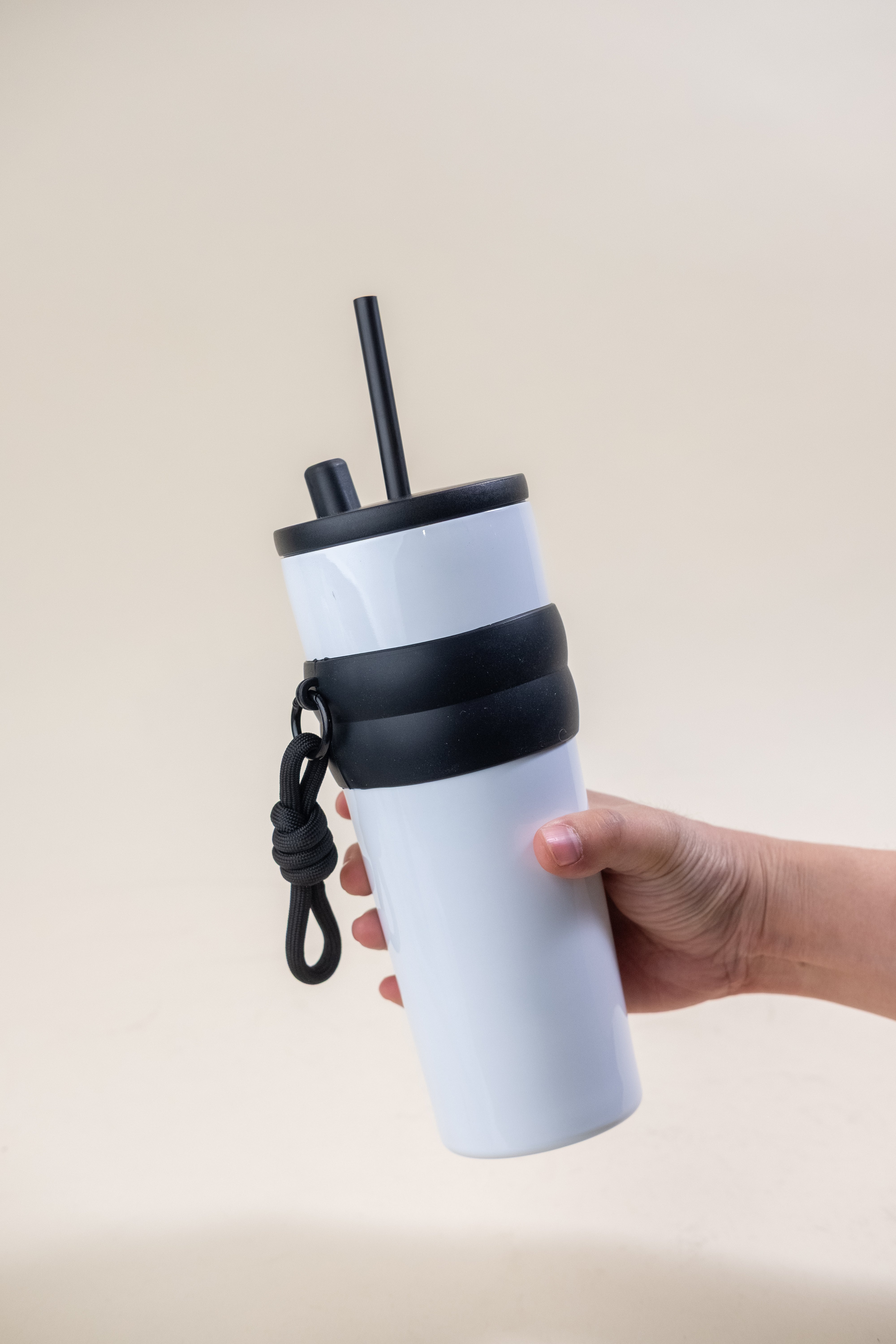 Close-up of a hand holding a two-tone stainless steel straw tumbler with a secure rubber grip and a BPA-free black plastic straw, designed for convenient daily use and easy portability. 