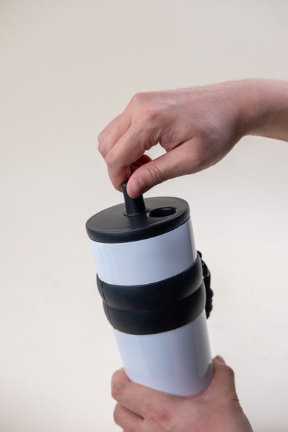 A person's hands securely fastening the lid on a white and black straw tumbler, demonstrating the tumbler's practical design for a leak-proof and secure drinking experience. 