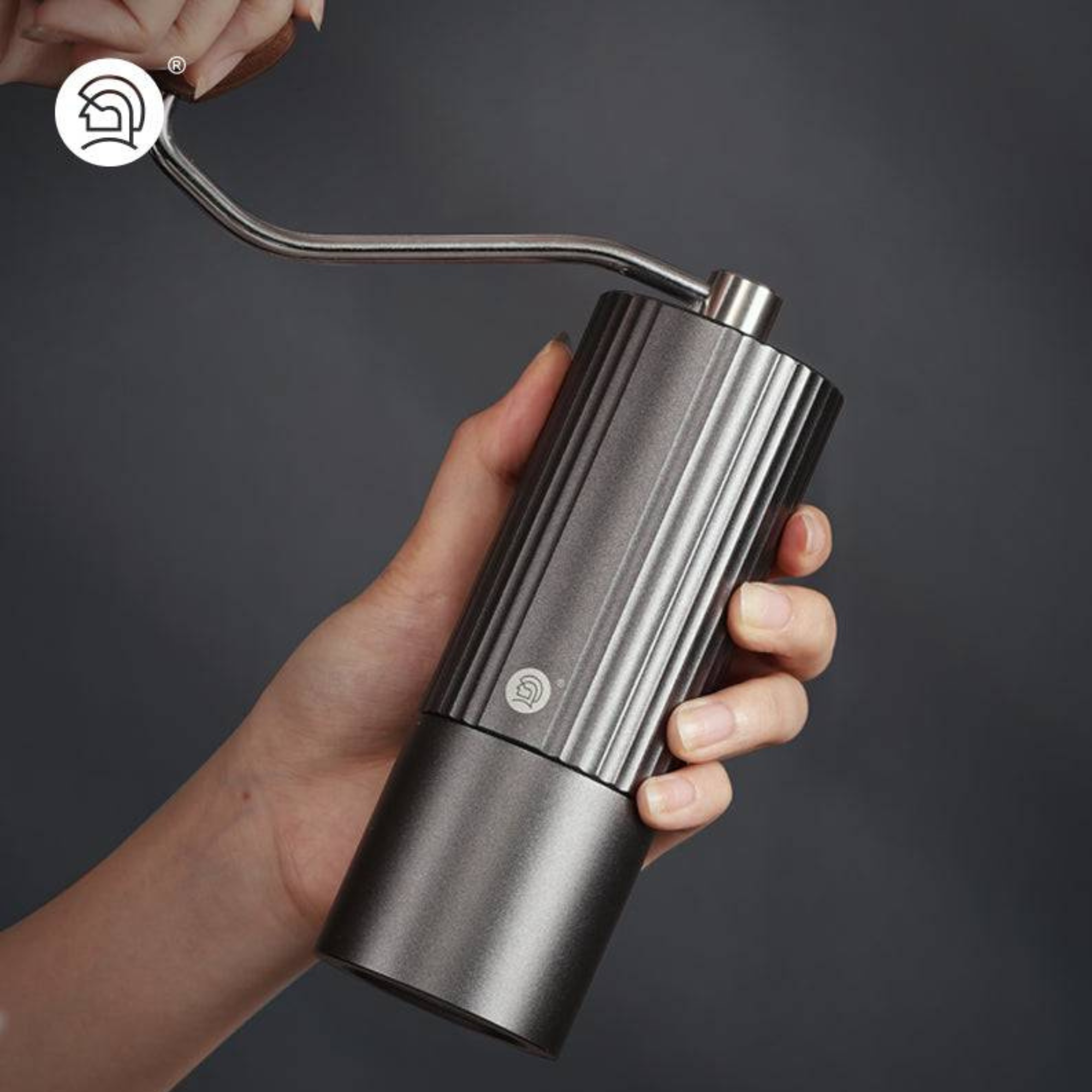 Hand holding a premium manual coffee grinder with stainless steel body and ergonomic wooden handle against a dark background