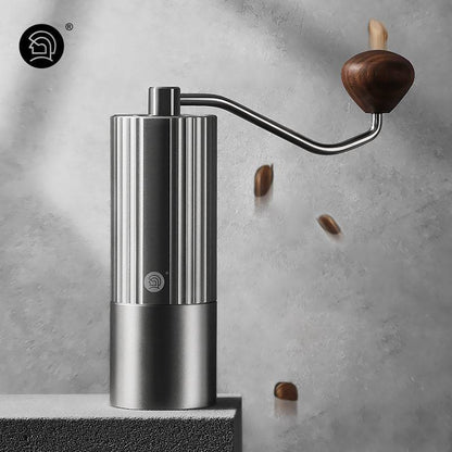 Modern stainless steel manual coffee grinder with a wooden handle, featuring a sleek ribbed design, set against a textured background with floating coffee beans