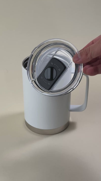 White insulated travel mug with a stainless steel base, featuring a spill-proof, sliding-lock lid being held by a hand.