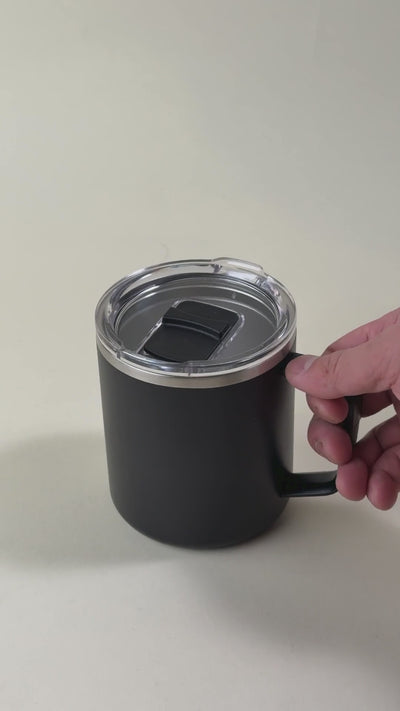 Black insulated coffee mug with a clear spill-resistant lid. Stainless steel mug with a handle, perfect for hot and cold beverages, featuring a secure sliding closure.