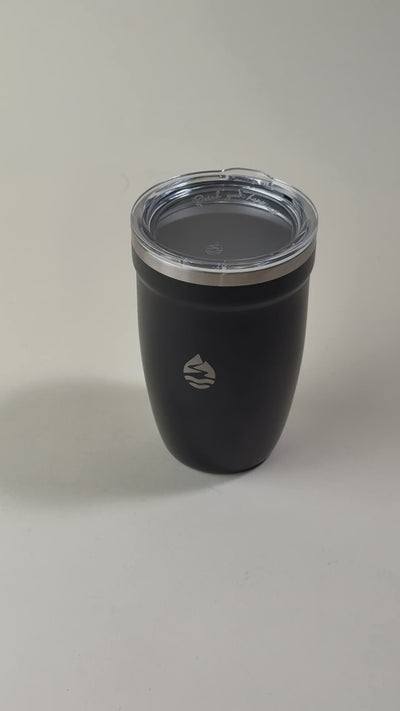 Hand holding a black insulated tumbler with a clear spill-resistant lid. Stainless steel travel mug designed to keep beverages hot or cold for extended hours.