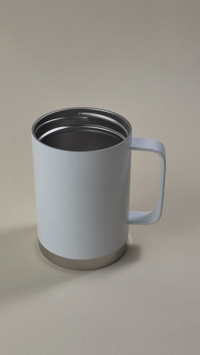 White insulated travel mug with a stainless steel base, featuring a spill-proof, sliding-lock lid being held by a hand.
