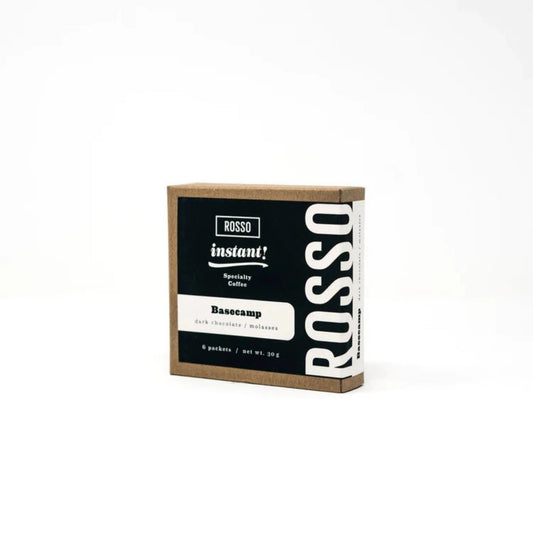 Rosso Coffee Roasters' Basecamp Instant Coffee: a rich blend with dark chocolate and molasses notes. Freeze-dried for flavor preservation. Six compostable packets per box. Ideal for travelers and adventurers.